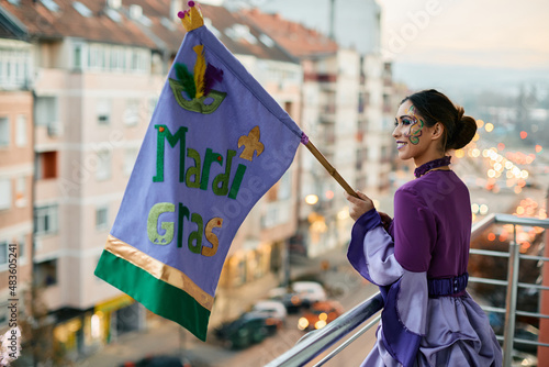 Young woman with Mardi Gras flag standing on balcony during celebration carnival.