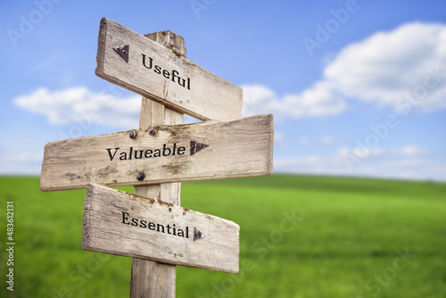 useful valueable essential text quote on wooden signpost outdoors on green field.