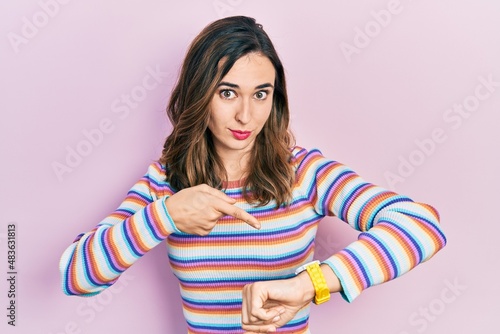 Young hispanic girl wearing casual clothes in hurry pointing to watch time, impatience, upset and angry for deadline delay