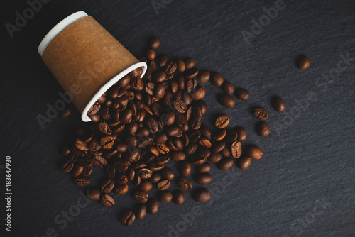 Coffee beans spilling from cup on granite