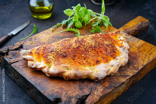 Traditional Italian pizza calzone with tuna fish and onions served as close-up on a rustic old wooden board