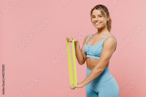Young happy strong sporty athletic fitness trainer instructor woman wear blue tracksuit spend time in home gym use fitness rubber bands isolated on pastel plain pink background. Workout sport concept.