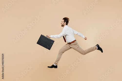 Full body side view young employee business man corporate lawyer 20s wear white shirt red tie glasses work in office jump run fast hold briefcase isolated on plain beige background studio portrait