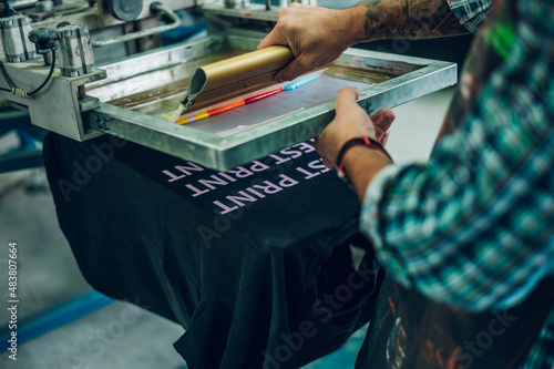 Male worker pressing ink on frame while using the printing machine in a workshop