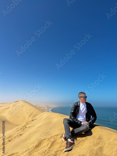 A young man sitting at sandy dunes on the seashore. Sandwich Harbour in Namibia