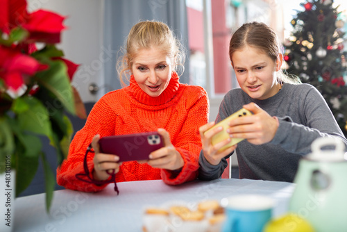 Mother and daughter together playing on their smartphones while sitting at the table at home during the celebration of christmas
