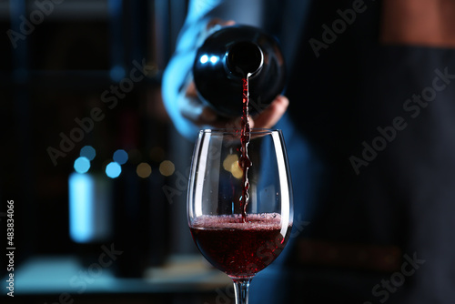 Bartender pouring red wine from bottle into glass indoors, closeup