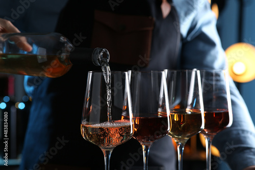 Bartender pouring rose wine from bottle into glass indoors, closeup