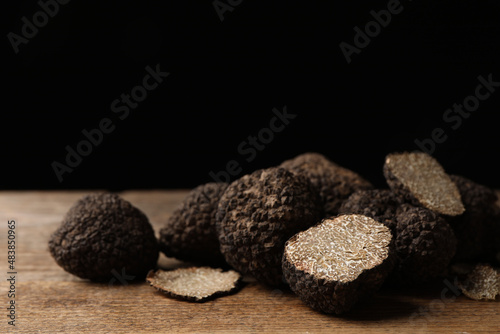 Whole and cut truffles on wooden table against black background, closeup