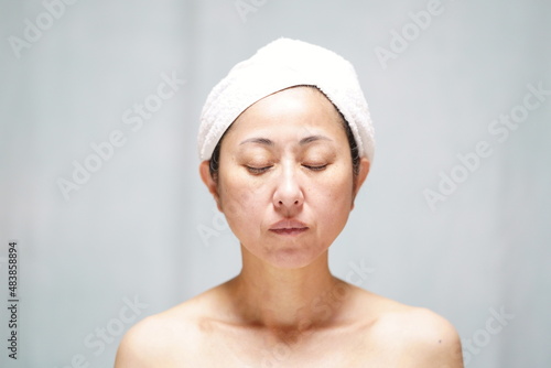 頭にタオルを巻いて目を閉じる素顔の中年女性 シミシワのある中年女性