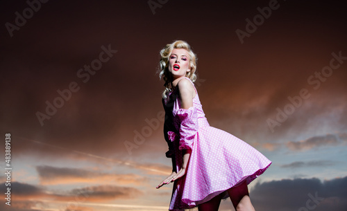 Woman in monroe dress on dramatic sky. Beautiful young woman wearing fashionable spring clothes. Portrait of the fashion model in trendy dress.