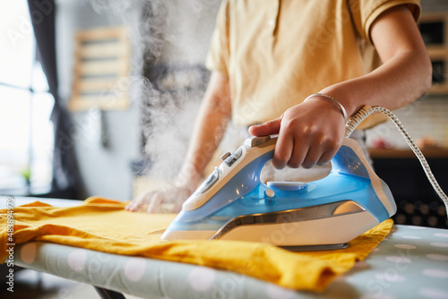 Close up of unrecognizable young woman ironing clothes at home, simple lifestyle and household chores concept, copy space