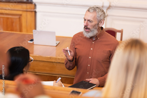 Mature professor holding chalk near multiethnic students in university