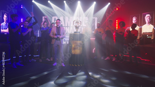 Host man speaking about golden cup while standing near cyber esportsmen at start of gaming tournament