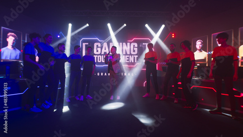 Group of teammates esport gamers walking and clapping hands then standing in front of monitor with gaming tournament banner at start of championship.