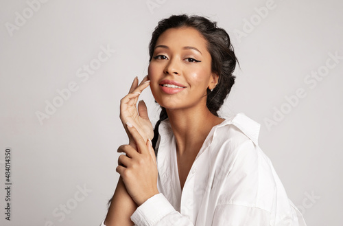 Beautiful mixed race young woman touch face enjoy perfect healthy smooth face skin, natural makeup. Pretty biracial female with ideal make-up posing on gray background. Skincare beauty cosmetics ad.