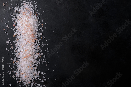Pink himalayan salt scattered and isolated on a black background, top view, flat lay, copy space