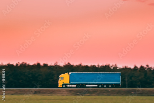 Yellow Truck Or Tractor Unit, Prime Mover, Traction Unit In Motion On Road, Freeway. Asphalt Motorway Highway Against Background Of Forest Landscape. Business Transportation And Trucking