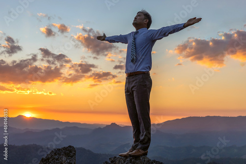 Successful businessman standing raised hand on top of peak mountain golden sunset background, success, competition and leader concept. Concept vision,