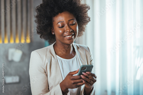 Young black businesswoman just arrived at the hotel taking a rest from a trip, using a smartphone. She working from hotel room on business trip, using smart phone. 