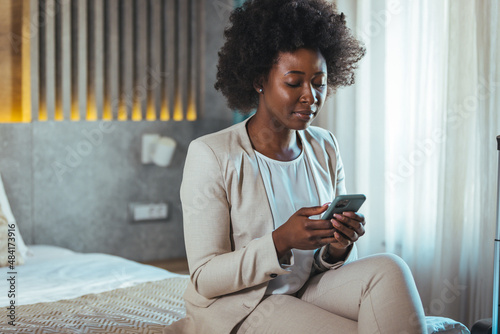 Young black businesswoman just arrived at the hotel taking a rest from a trip, using a smartphone. She working from hotel room on business trip, using smart phone. Hotel, Lobby, Relaxation