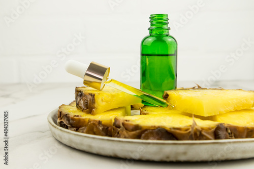 face serum with pineapple extract and collagen in a cosmetic bubble and pipette dispenser against the background of ripe pineapple slices.