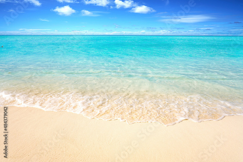 Beautiful sandy beach with white sand and rolling calm wave of turquoise ocean on Sunny day. White clouds in blue sky. Perfect tropical seascape, copy space.