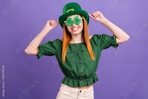 Photo of shiny charming young lady wear green blouse cap celebrating st patrick day smiling isolated purple color background