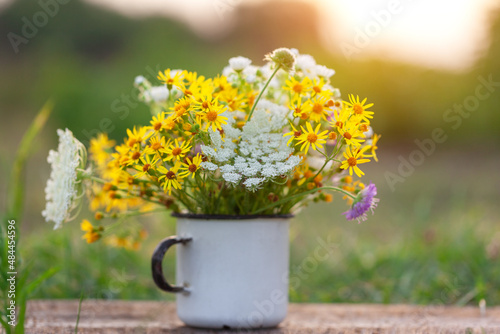 Beautiful wild flowers in white cup on wooden table and nature background.