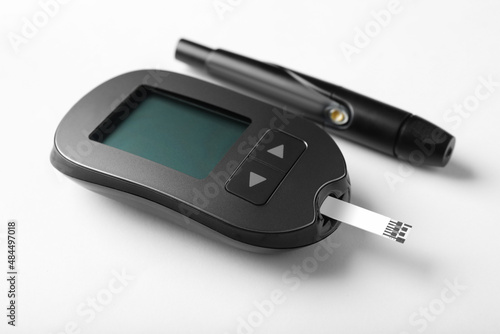 Digital glucometer with test strip and lancet pen on white background. Diabetes control