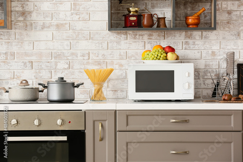 Modern microwave oven on counter near light brick wall in kitchen