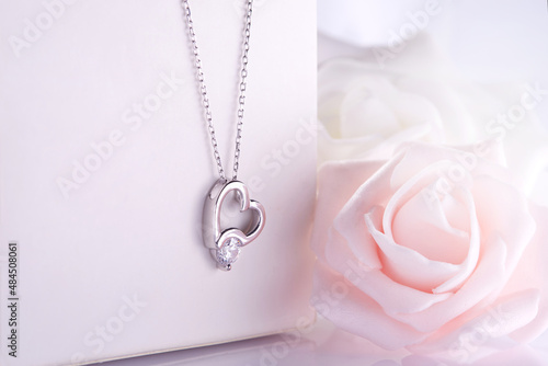 Diamond heart necklace hanging on white jewelry box soft roses in background