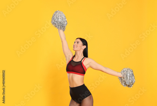 Beautiful cheerleader in costume holding pom poms on yellow background