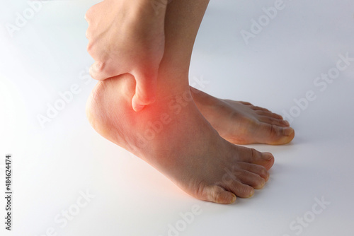 A person holding ankle on Achilles tendon, suffering with pain in red spot area. Sprain ligament or Achilles tendonitis symptoms. Image with red highlights on hurting area, Health care concept