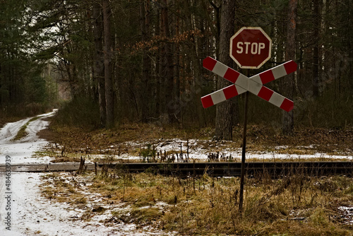Znak stop i krzyż świętego Andrzeja przed przejazdem kolejowym w lesie zimą . Tory kolejowe , leśna droga śnieg.