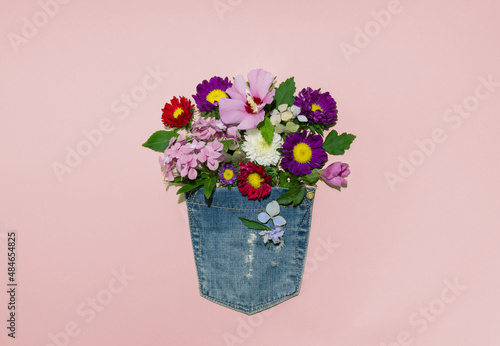Blooming summer flowers in a jeans pocket against pastel pink background. Minimal creative idea flat lay.