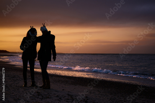 Sylwetki, kontury, zarysy postaci dziewczęcych na morskiej plaży na tle nastrojowego zachodu słońca. Silhouette