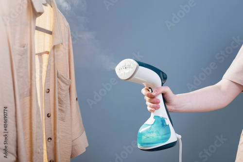 female hand with steamer and shirt on blue background