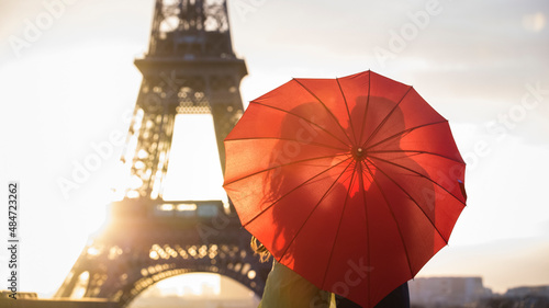 Romantic kiss at the Eiffel tower with a red umbrella during sunrise