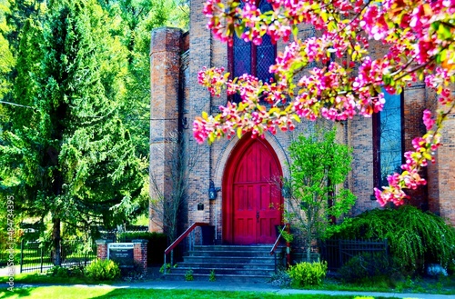 Old church building with elegant red door. The St Paul's Episcopal Church in Montour Falls, New York, a historic brick building by Charles COOK in 1853. Blurred foreground of red flowers