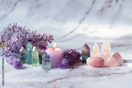 Gemstones minerals, candle, lilac flowers on marble background. Healing stones for Crystal Ritual, esoteric spiritual practice, aura cleansing, relax. reiki therapy. Fluorite, amethyst, rose quartz