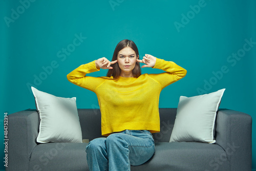 Irritated young girl close, plug ears, ignoring loud sound or noise, sitting on sofa, annoyed by noisy neighbors