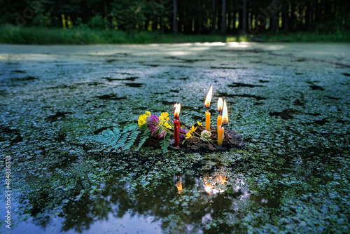 flowers and burning candles on dark water, covered aquatic plants duckweeds (Lemna). old tradition, fortune telling for pagan holiday. Summer Solstice Day, Midsummer, wicca, Litha sabbat