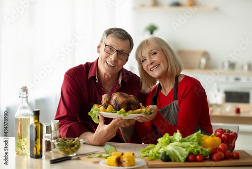 Portrait of happy senior couple holding dish with tasty roasted turkey for family Christmas celebration at kitchen