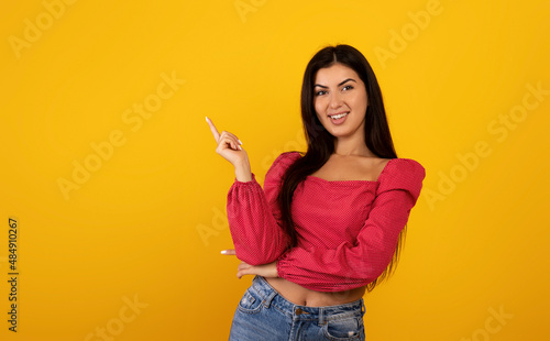 Look here. Portrait happy armenian lady pointing finger aside at free space advertising your text, yellow studio background