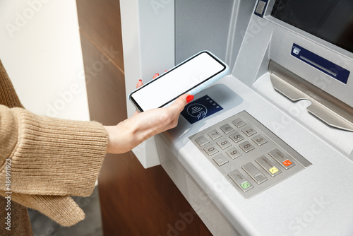 Female hand with mobile phone withdrawing money from atm using NFC contactless wi-fi pay pass system.