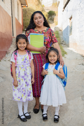 Hispanic mom and daughters ready to go to school - Latin mom accompanying her daughters to school - Hispanic girls with backpack outside their house in rural area
