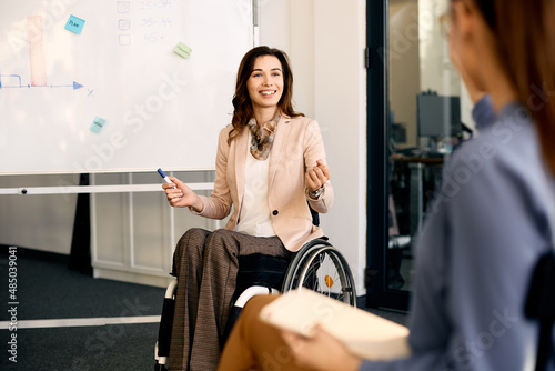 Happy entrepreneur in wheelchair explains inclusive business strategy to her coworkers during presentation in meeting room.