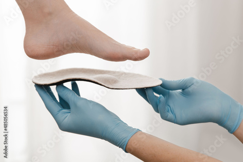Orthopedic insole on a white background. Hands in rubber gloves hold an orthopedic insole. Foot care, comfort for the feet. Doctor orthopedist tests the medical device. Flat feet correction