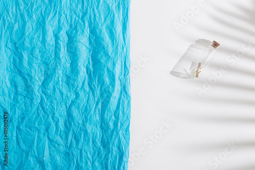Message in a bottle with palm leaf shadow and blue crepe paper on beige background. Summer, vacation Love or Valentine's Day concept. Flat lay.